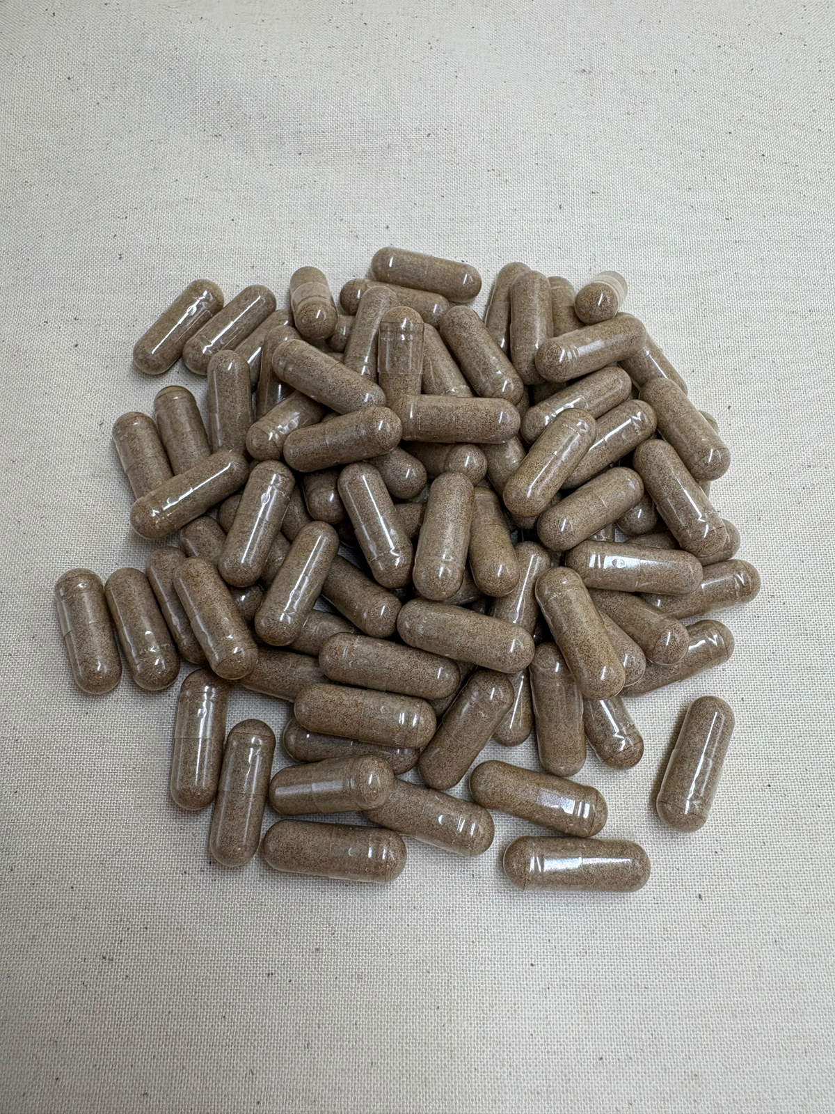 A pile of brown herbal supplement capsules on a textured off-white fabric background.