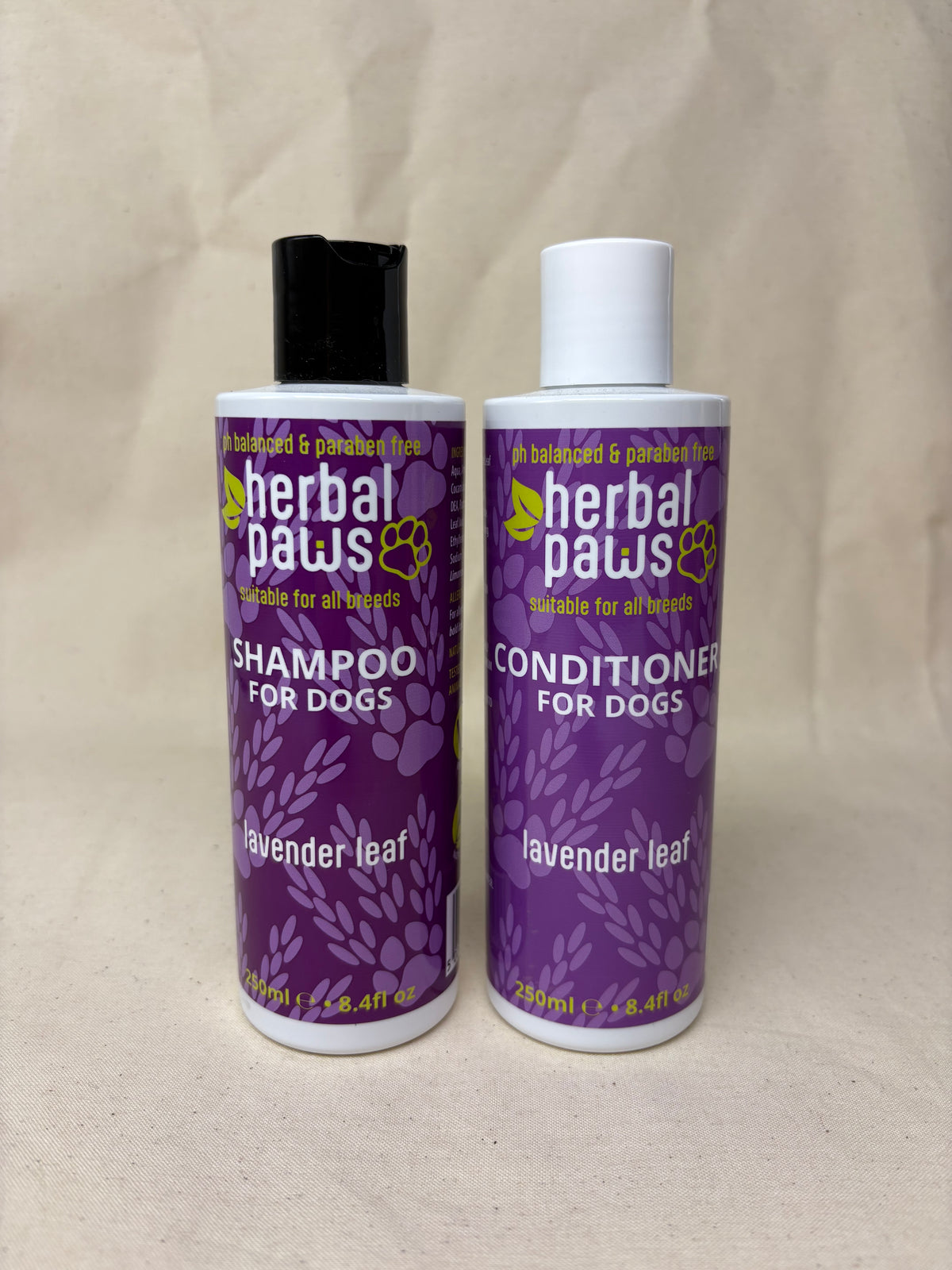 Two bottles of Herbal Paws pet shampoo and conditioner for dogs, labeled lavender leaf, shown on a beige fabric background.