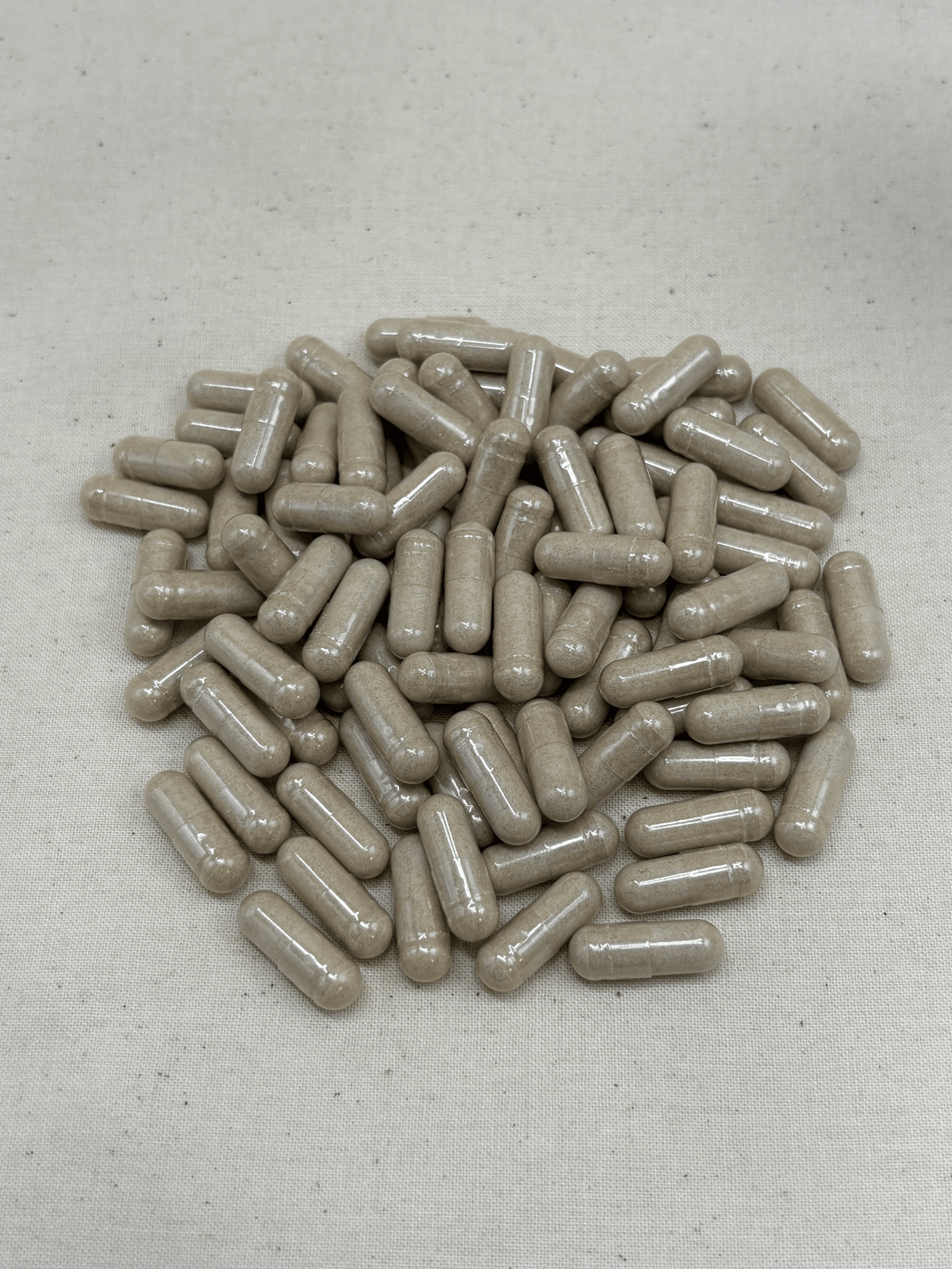 A pile of beige turkey tail mushroom capsures, a herbal supplement capsules on a light beige textured fabric background by Herbal Paws UK