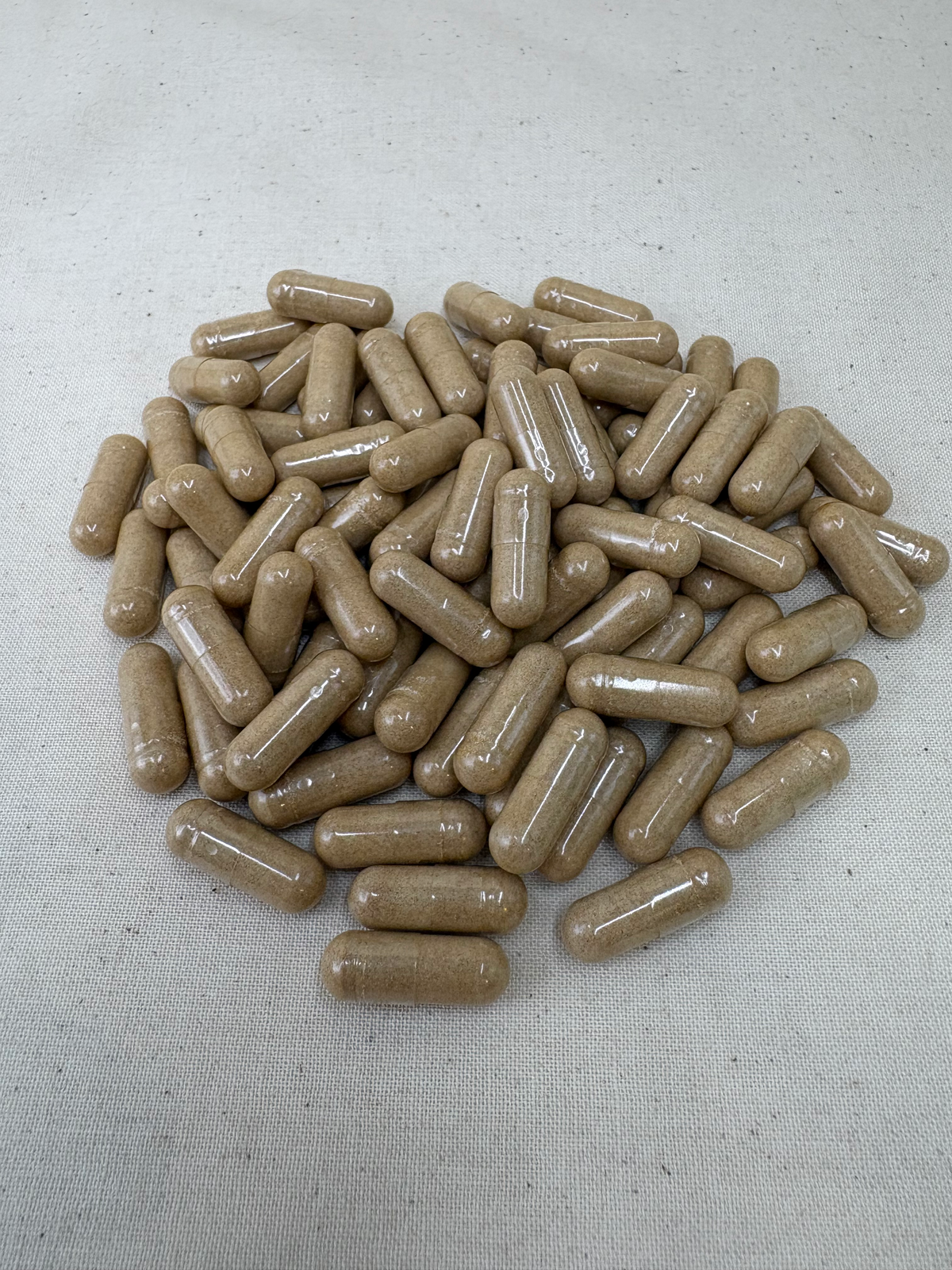 A pile of tan-brown herbal supplement capsules on a light beige textured fabric background representing corcydeps mushroom capsules for dogs