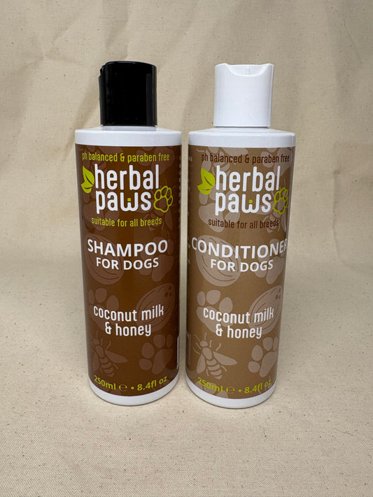 Two bottles of Herbal Paws Coconut Milk & Honey dog shampoo and conditioner, shown side-by-side on a beige fabric background.