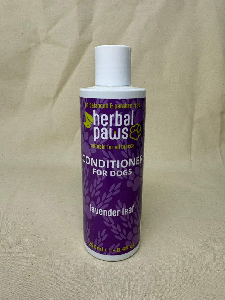 A bottle of Herbal Paws Conditioner for Dogs, lavender leaf scent, with a purple label and white cap, set against a beige fabric background.