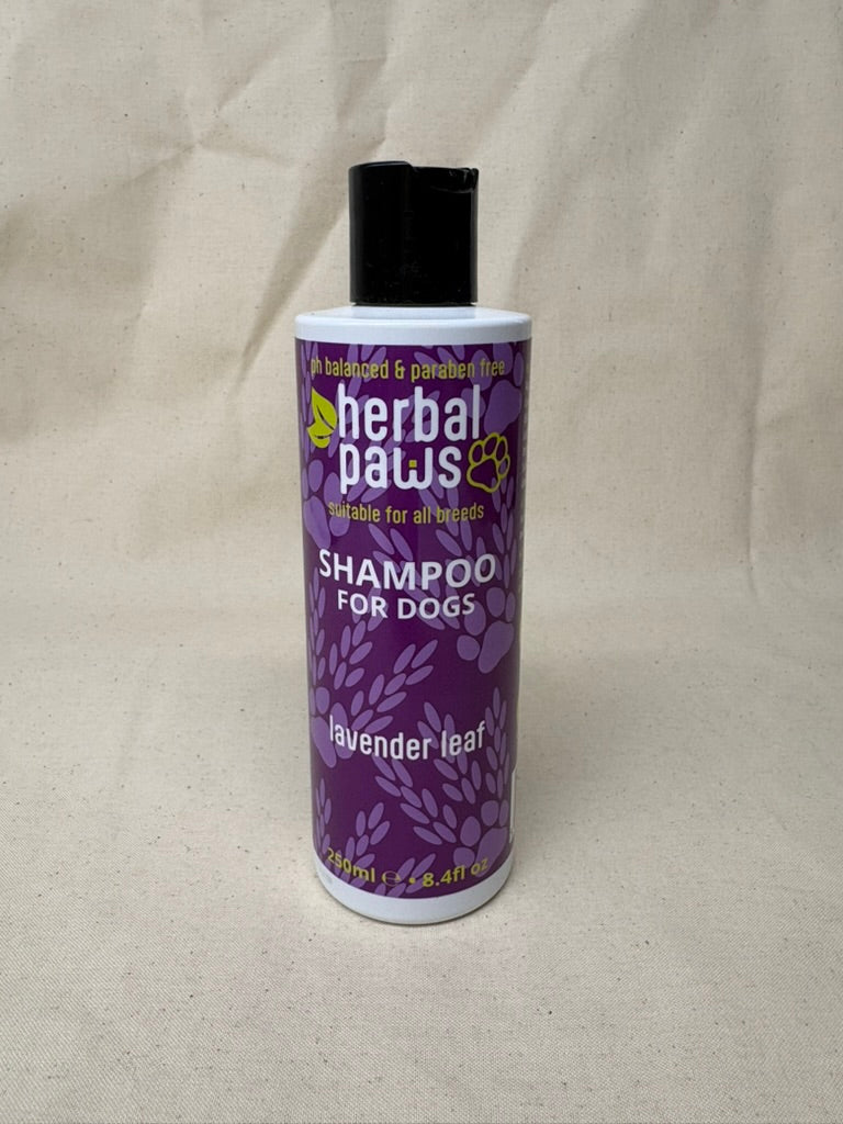 A bottle of Herbal Paws Shampoo for Dogs, lavender leaf scent, with a purple and white label and a black cap, set against a neutral beige fabric background.