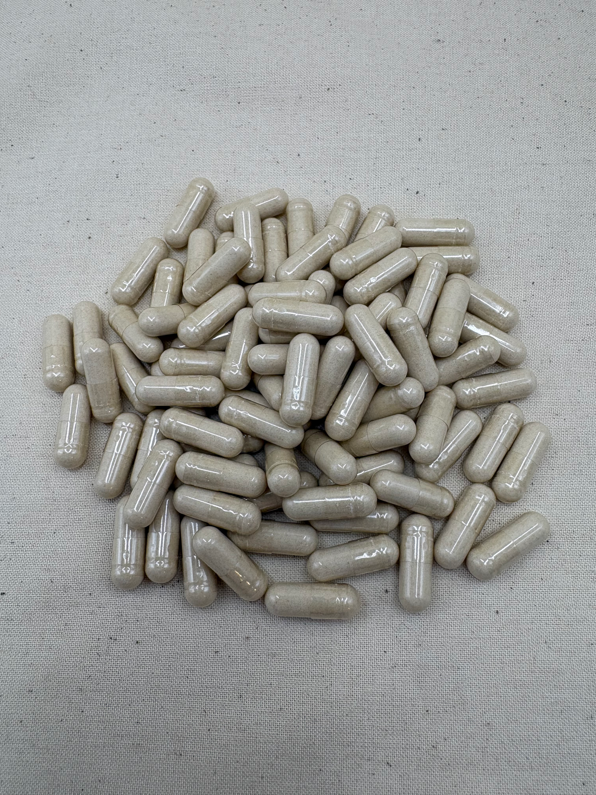 A pile of beige herbal supplement capsules on a light beige textured fabric background.