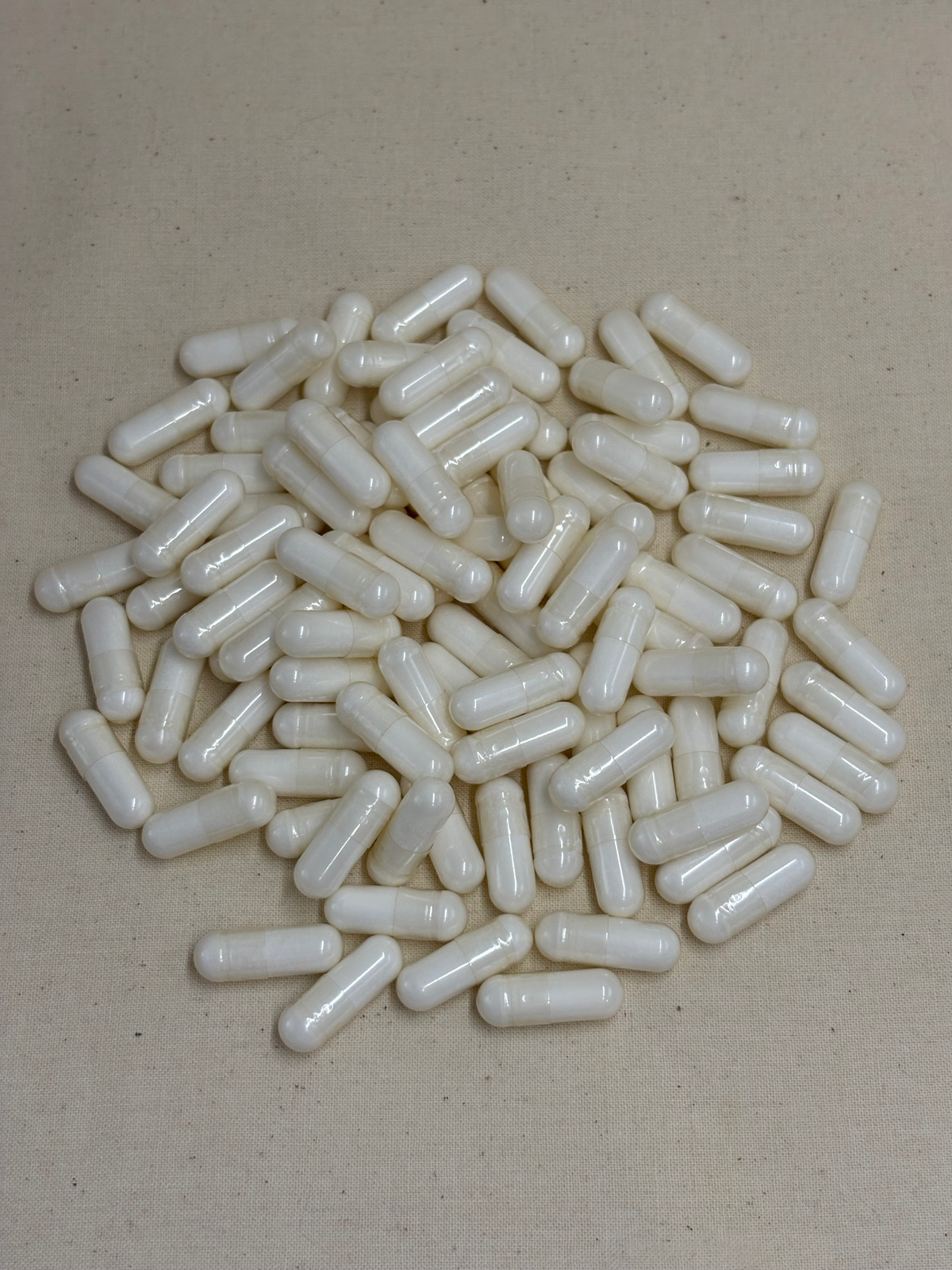 A pile of white translucent capsules or gelatin capsules scattered on a light beige fabric background.