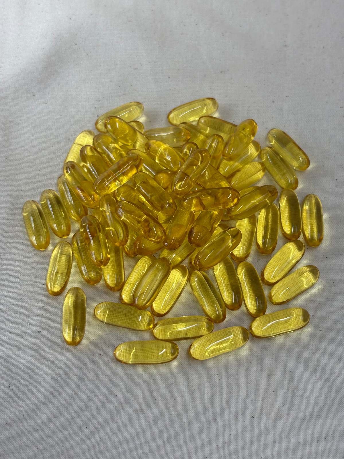 A pile of translucent yellow softgel capsules on a light gray fabric background.
