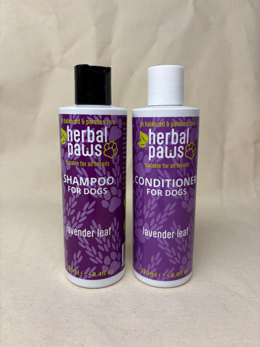 Two bottles of Herbal Paws pet shampoo and conditioner for dogs, labeled lavender leaf, shown on a beige fabric background.